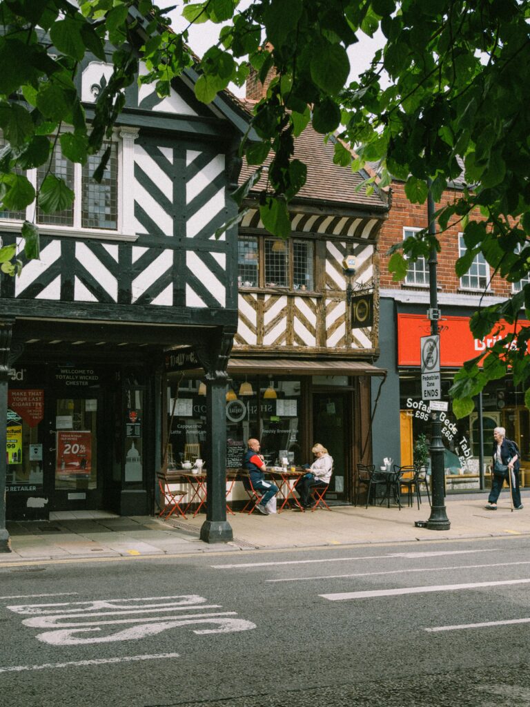A picturesque street in Chester, England, featuring Tudor-style buildings and outdoor café seating.