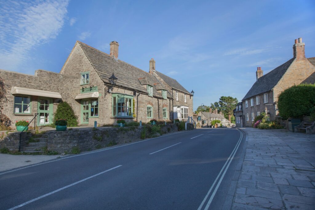 Quaint village street with historic stone buildings in Dorset, England under a clear blue sky.